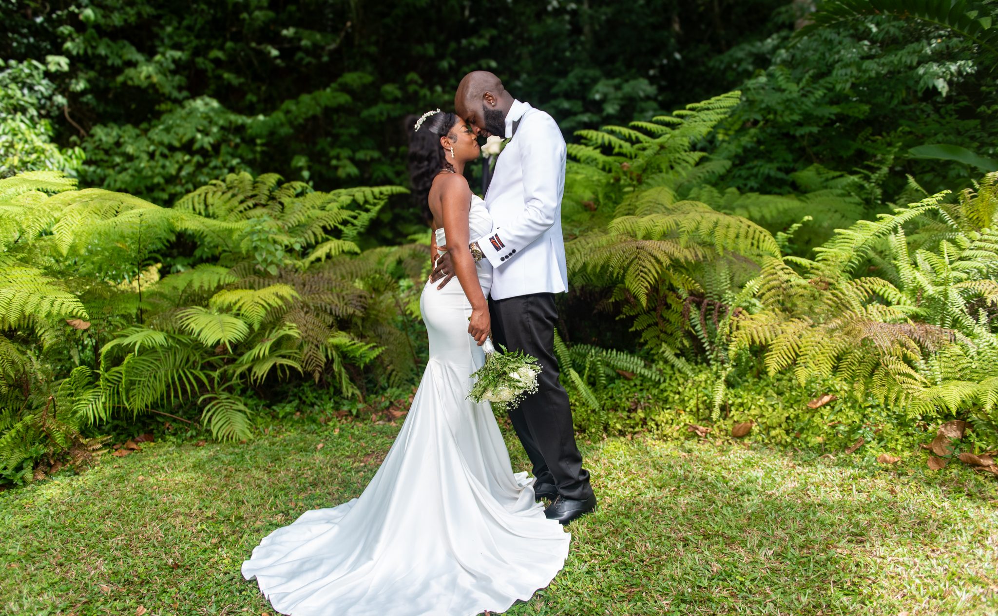A bride and groom stand forehead to forehead among tree ferns
