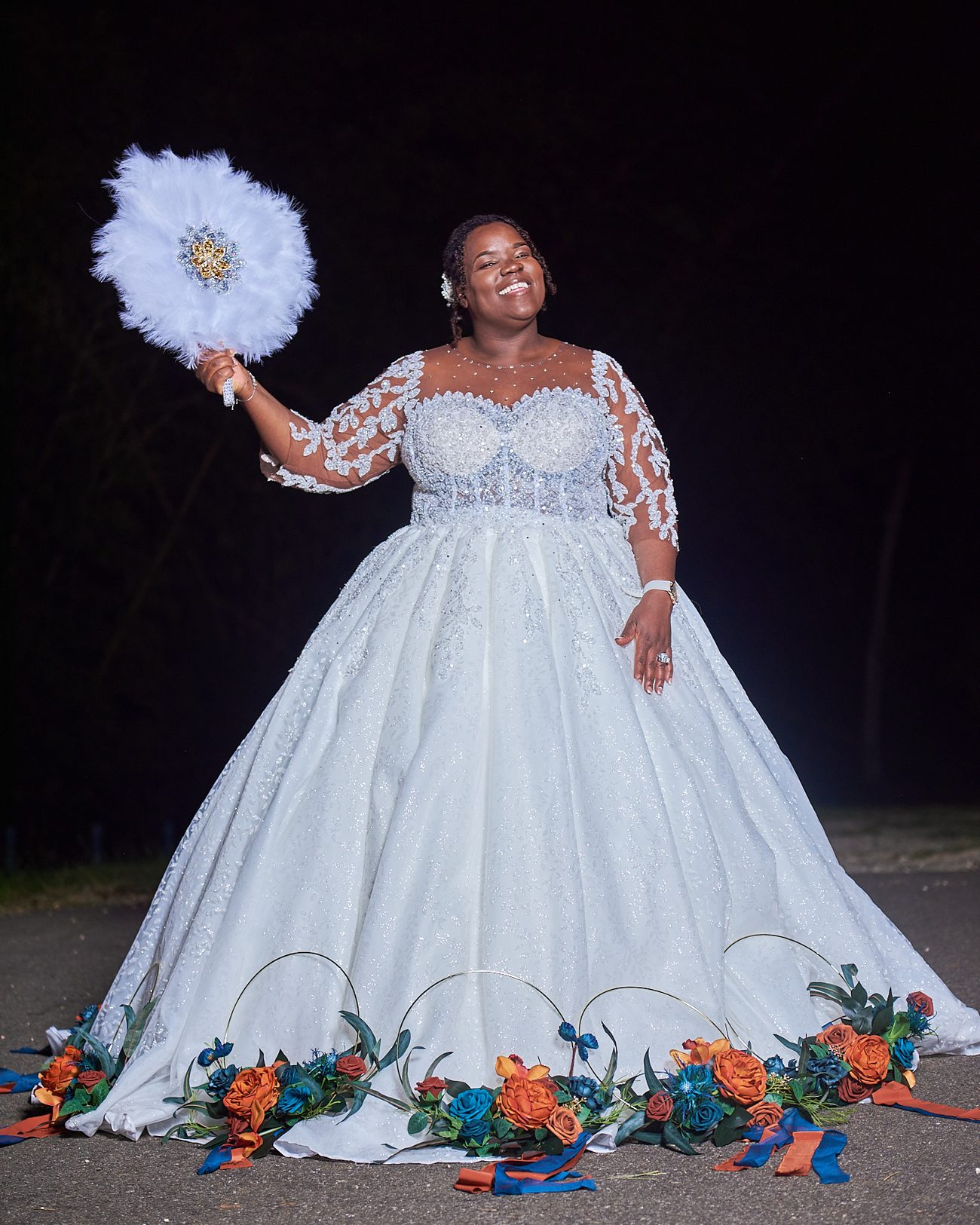 A bride in a sequinned ballgown holding a feather fan at night